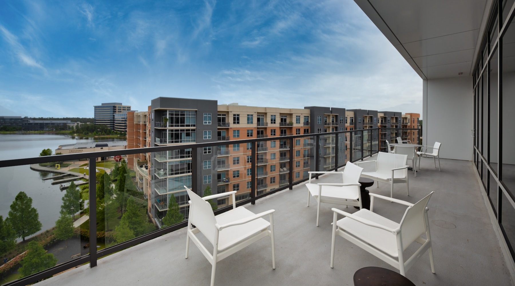 a large patio with seating glass railing and view of another building and a body of water