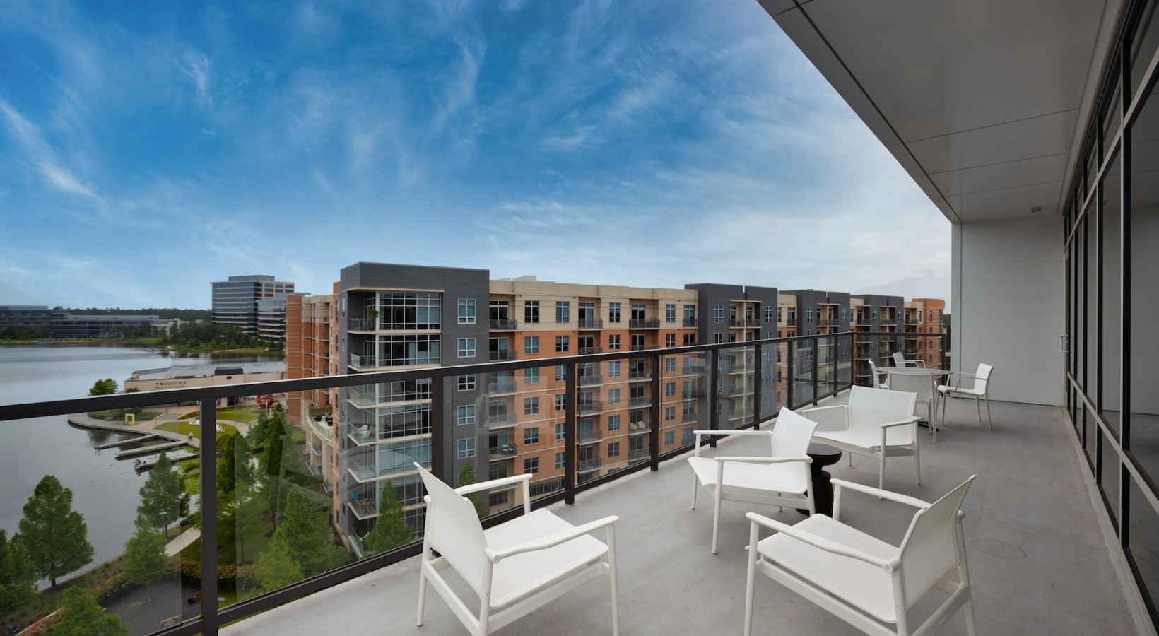 a large patio with seating glass railing and view of another building and a body of water