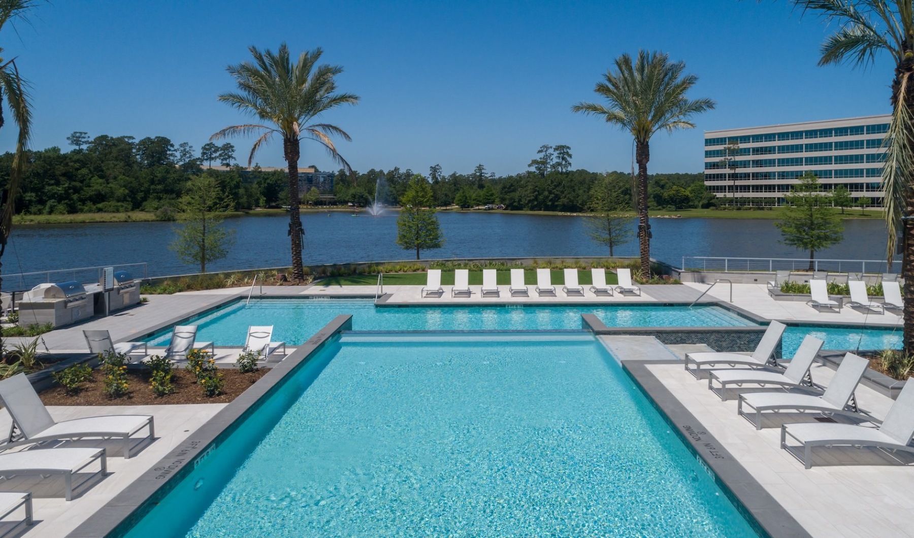 resort style pool with seating palm trees and a larger body of water behind it