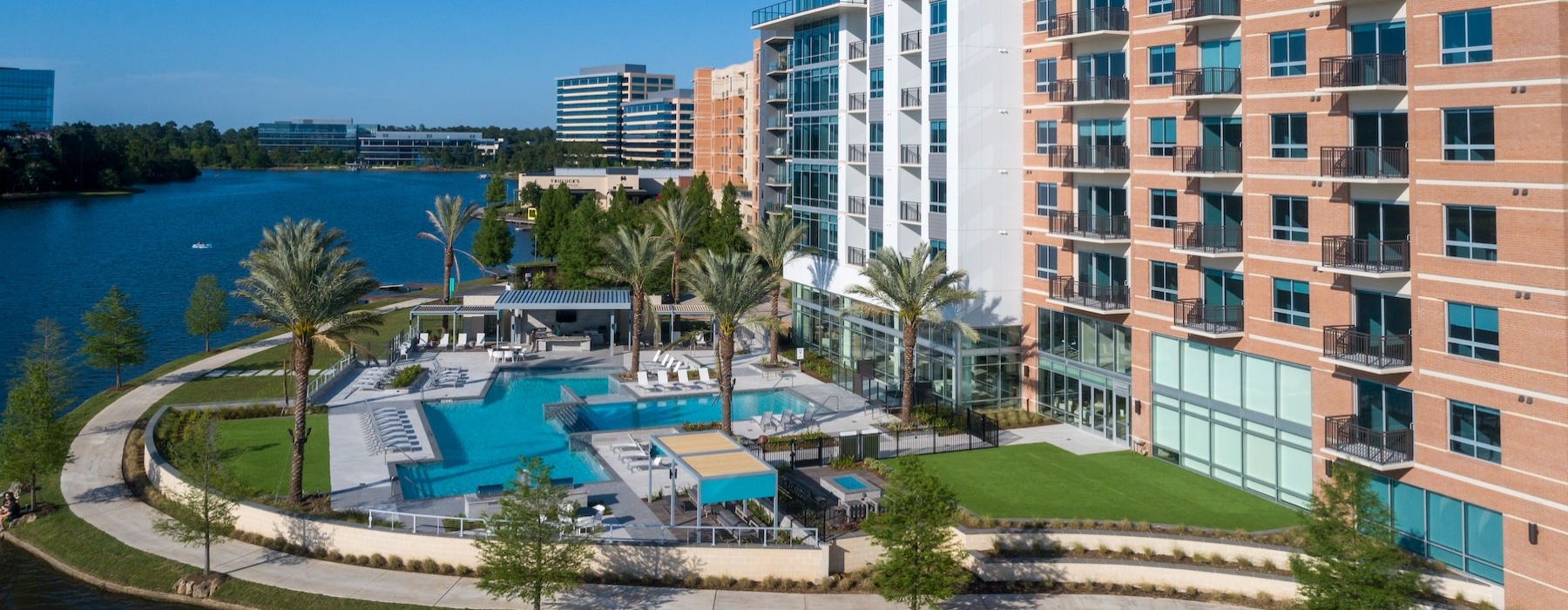 a large building with a pool palm trees and larger body of water in front of it